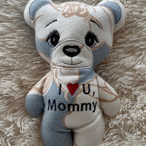 May include: A handmade teddy bear with a white, blue, and tan floral pattern. The bear has embroidered black eyes and a black nose. The text "I U, Mommy" is embroidered on the bear's chest, with a red heart replacing the word "love".