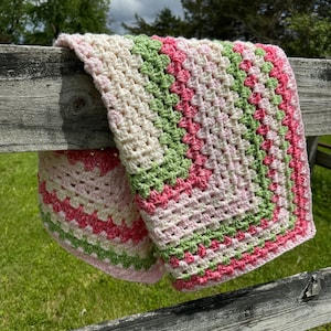 May include: A crocheted baby blanket with a white background and stripes of pink and green.