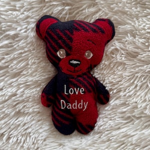 May include: A handmade teddy bear with a red and black striped pattern. The bear has embroidered eyes and a stitched nose and mouth. The words "Love Daddy" are embroidered on the bear's chest.