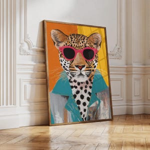 Op de afbeelding: Een ingelijste kunstdruk van een luipaard met een felroze zonnebril en een jas met een blauwgroene kraag. De achtergrond is verdeeld in verticale oranje en gele vlakken. De luipaard heeft zwarte vlekken op een crèmekleurige vacht.
