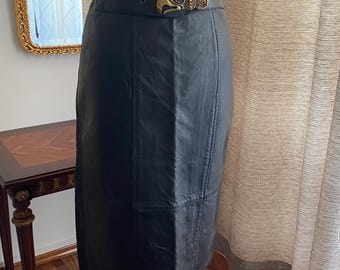 May include: A black leather skirt with a high waist and a decorative belt. The belt has a gold-coloured buckle with an ornate design. The skirt is knee-length and has visible stitching details.