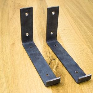 Puede incluir: Dos soportes de estante de metal negro con un ángulo de 90 grados. Los soportes están hechos de metal resistente y tienen varios agujeros para montaje.