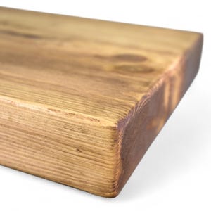 Peut inclure: Gros plan sur une &eacute;tag&egrave;re rectangulaire en bois avec une finition marron chaud et naturelle. Le grain du bois est visible et les bords ont une apparence l&eacute;g&egrave;rement plus fonc&eacute;e et br&ucirc;l&eacute;e. L'&eacute;tag&egrave;re est probablement pour la d&eacute;coration int&eacute;rieure.
