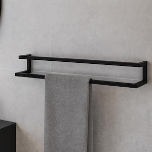 Może przedstawiać: Czarny, podwójny wieszak na ręczniki zamontowany na jasnoszarej, kafelkowanej ścianie. Szary ręcznik wisi na wieszaku. Armatura łazienkowa ma minimalistyczny design. Czarna bateria i okrągłe lustro są widoczne w tle.