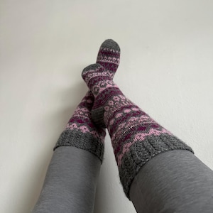 May include: A pair of grey and pink patterned socks with a grey cuff. The socks are worn on a person's legs, with the feet crossed.
