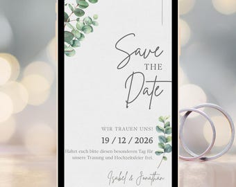 May include: A smartphone screen displays a wedding invitation with the text "Save the Date." The design includes green eucalyptus leaves and the date 12/19/2026. Two silver wedding bands are in the background.