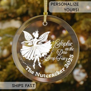 May include: A clear, round Christmas ornament with a gold ribbon. The ornament features a white illustration of a fairy and the text "Sophie as the Dew Drop Fairy 2025" and "The Nutcracker". The text "Personalize Yours!" is at the top.
