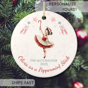May include: A round white ceramic Christmas ornament featuring a ballerina in a red and white tutu holding a candy cane. The design includes pink ballet slippers, stars, and snowflakes. Text reads: THE NUTCRACKER 2025 and Olivia as a Peppermint Stick.