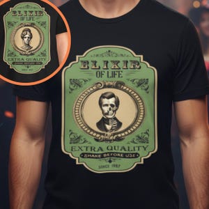 May include: Black t-shirt featuring a green and beige graphic with the text "ELIXIR OF LIFE." The graphic includes a portrait of a man with a skull face and the words "EXTRA QUALITY" and "SHAKE BEFORE USE." The shirt design is vintage-inspired.
