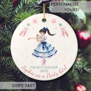 May include: Round Christmas ornament featuring a ballerina holding a doll, with the text "The Nutcracker 2025 Sophie as a Party Girl." The ornament has a gold string for hanging, with pink stars, snowflakes, and ballet slippers.