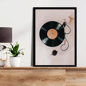May include: A framed print of a black vinyl record playing on a turntable. The record is on a white background with a black frame.