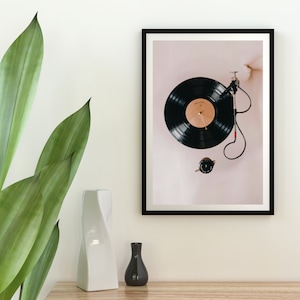 May include: A framed black and white photograph of a black vinyl record on a turntable. The record is playing and the needle is visible. The background is a light pink.