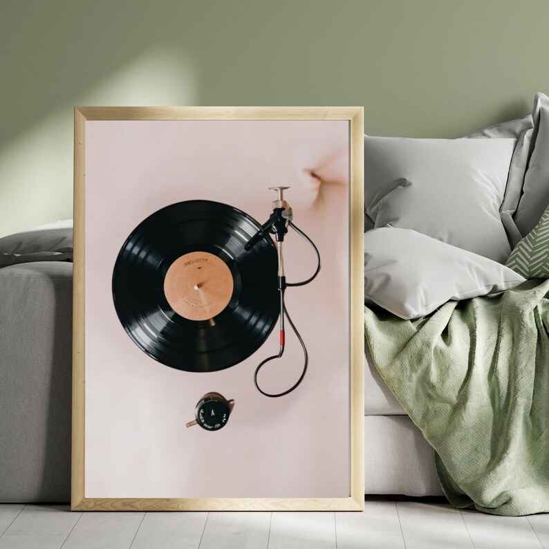 May include: A framed print of a vintage record player with a black vinyl record on the turntable. The record player is on a light pink background.