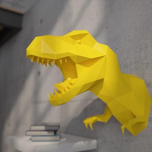 Puede incluir: Una cabeza de dinosaurio de origami amarilla montada en una pared. El dinosaurio tiene una gran boca abierta con dientes afilados.