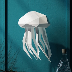 Könnte beinhalten: Ein weißer Papier-Medusen-Mobile, der an einer türkisfarbenen Wand hängt. Die Meduse besteht aus gefaltetem Papier und hat einen 3D-Effekt.