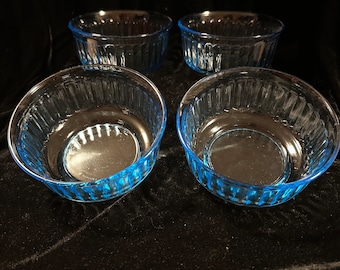 May include: Four clear glass bowls with a light blue rim. The bowls are all the same size and shape, and they are arranged in a row.