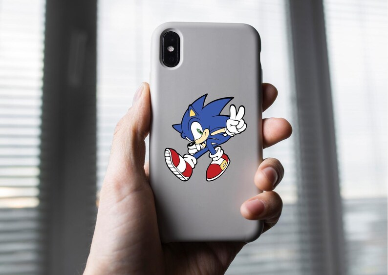 May include: A white phone case with a blue and red Sonic the Hedgehog sticker. Sonic is running and giving a peace sign.