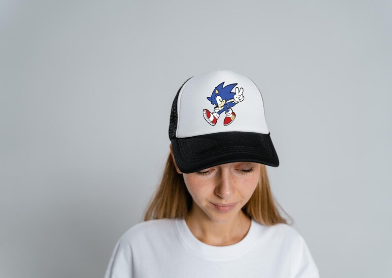 May include: A white and black trucker hat with a blue Sonic the Hedgehog graphic. The graphic shows Sonic running with his arms raised and a peace sign.