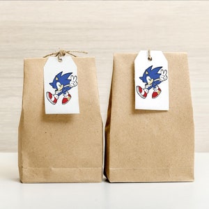 May include: Two brown paper gift bags with white tags. Each tag has a cartoon image of Sonic the Hedgehog, a blue hedgehog with red shoes, running and giving a peace sign.
