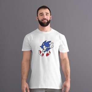 May include: A white t-shirt with a blue and red cartoon character of Sonic the Hedgehog. Sonic is running and giving a peace sign.