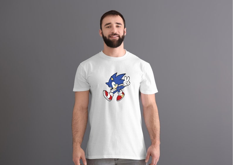 May include: A white t-shirt with a blue and red cartoon character of Sonic the Hedgehog. Sonic is running and giving a peace sign.