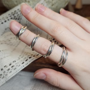 May include: A hand displaying several silver rings. The rings feature a twisted, rope-like design. The rings are worn on different fingers, highlighting the style. The background is blurred, with a textured surface and lace fabric.