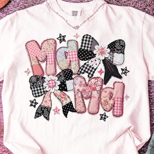 Puede incluir: Camiseta rosa claro con la frase "Ma Kind" en un diseño de patchwork. Las letras y los lazos están decorados con estampados florales, de cuadros y paisley. La camiseta tiene cuello redondo y mangas cortas.