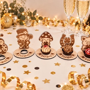 May include: Five circular wooden stands with laser-engraved designs including a ladybug, a person in a top hat, a mushroom, a horseshoe, and a pig. Each stand features the text "Viel Gl&uuml;ck" and a circular cutout for holding small round treats.