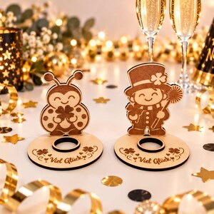 May include: Two wooden stands featuring laser-cut designs of a ladybug and a person in a top hat, each holding a four-leaf clover. Both circular bases are engraved with the German text Viel Gl&uuml;ck and include a central hole for holding items.