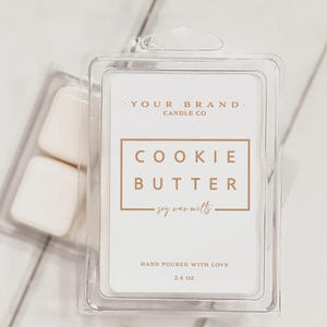 May include: A clear plastic container holding soy wax melts. The label reads "COOKIE BUTTER" and "soy wax melts." The label also states "HAND POURED WITH LOVE" and "2.4 OZ." The brand name is "YOUR BRAND CANDLE CO."