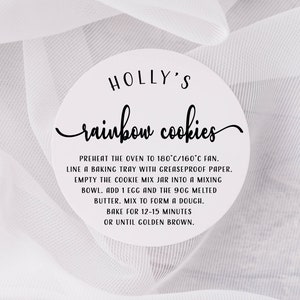 May include: A white circular sticker with black text that reads "HOLLY'S rainbow cookies". The sticker includes instructions for baking rainbow cookies, including preheating the oven to 180&deg;C/160&deg;C fan, lining a baking tray with greaseproof paper, adding an egg and melted butter to the cookie mix, and baking for 12-15 minutes.