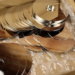 Könnte beinhalten: Eine Schachtel gefüllt mit Luftpolsterfolie und einem großen Stapel glänzender, silberner, runder Metallscheiben. Die Scheiben haben ein Loch in der Mitte.