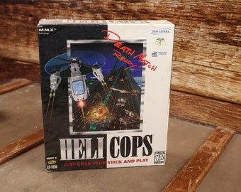 Può includere: Una scatola bianca con un'immagine in bianco e nero di un elicottero che vola sopra una città. La scatola è per un videogioco chiamato "Heli Cops" e dice "Just grab your stick and play".