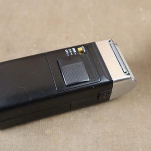 以下が含まれることがあります： 銀色のヘッドと日立Mr. Slimのラベルが付いた黒い電気シェーバー。シェーバーには電源スイッチとスライド式のオン/オフスイッチがあります。