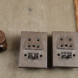 May include: Three vintage brown electrical outlets with switches. The outlets have two round holes and a rectangular slot. The switches are black and have a toggle design.