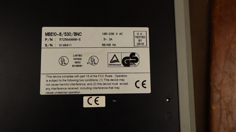 May include: A black metal box with a label that reads "MBE10-8/530/BNC" and includes the part number, serial number, and voltage and amperage specifications. The label also includes safety certifications from UL, GS, and CE.
