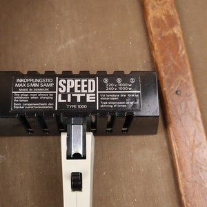 May include: Black Speed Lite Type 1000 flash unit with a white power switch and a label that reads "Inkkopplingstid Max 5 Min 5 Amp Made in Denmark 220 v 1000 w 240 v 1000 w. Vid lampbyte dra f&ouml;rst ur stickkontakten Trak str&ouml;mkabeln ur f&ouml;rst ur stickkontakten af lampan."