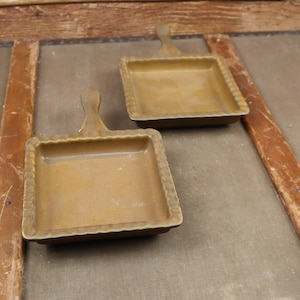 May include: Two square ceramic dishes with handles. The dishes are a light brown color and have a textured rim.