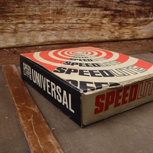 May include: A vintage box of Speedlite Universal flashbulbs. The box is brown with red and white concentric circles and the text "Speedlite Universal" in black letters.