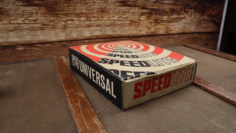 May include: A vintage box of Speedlite Universal flashbulbs. The box is brown with red and white concentric circles and the text "Speedlite Universal" in black letters.