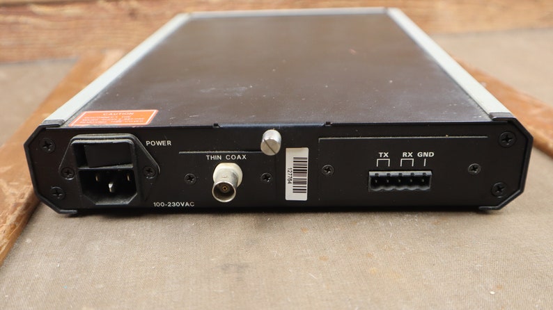 May include: Black electronic device with a power cord, a thin coax connector, and a 6-pin connector labeled "TX", "RX", and "GND". The device has a label that reads "100-230VAC".