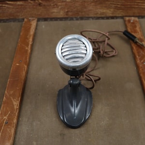 May include: A vintage black and silver microphone with a round, grill-covered speaker and a black base. The microphone is connected to a cord with a plug.