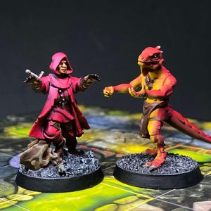 May include: Miniature figurines of a robed figure with a sword and a lizard-like humanoid. The figures are painted in shades of red, orange, and yellow, set on black bases. The background is a dark gradient.