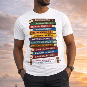 Könnte beinhalten: Weißes T-Shirt mit einem Stapel bunter Bücher, die inspirierende Sätze wie "Dream Like Martin" und "Lead Like Harriet" tragen. Enthält ein Zitat von A. Philip Randolph.