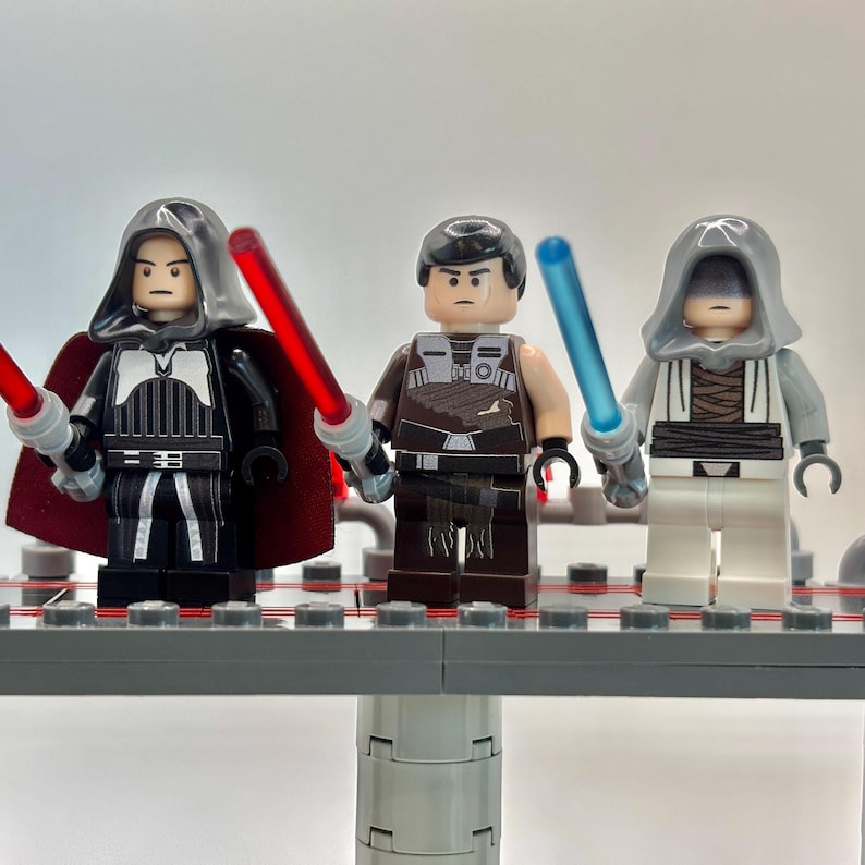 May include: Three Star Wars Lego minifigures, one with a red lightsaber, one with a blue lightsaber, and one with a gray hooded robe.