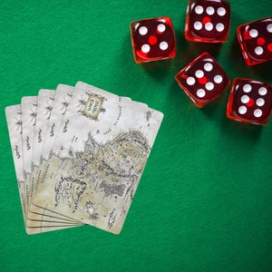 May include: A collection of playing cards with a detailed map design, fanned out on a green surface. Six red dice with white dots are scattered around the cards, suggesting a game or tabletop activity.