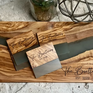 May include: A set of three wooden coasters with a gray epoxy resin inlay. Each coaster features the text "The Buettners EST. 2022" in a cursive font.