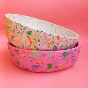 Könnte beinhalten: Zwei Keramikschalen, eine weiße und eine rosa, mit einem gesprenkelten Muster aus bunten Punkten. Die Schalen sind übereinander gestapelt.