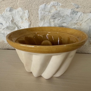 Puede incluir: Un molde para bizcocho de cerámica vintage con exterior color crema e interior y borde amarillo dorado. El molde tiene un diseño acanalado y un tubo central, perfecto para hornear pasteles y postres.