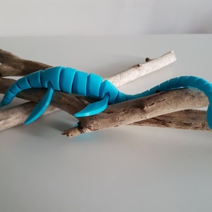 Peut inclure: Un dinosaure en plastique bleu vif, ressemblant à un plésiosaure, est posé sur un ensemble de branches de bois flotté.